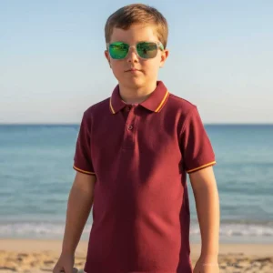 Niño con polo granate y detalles de la bandera de España junto al mar